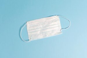 A disposable face mask lying on a light blue surface, symbolizing health protection.